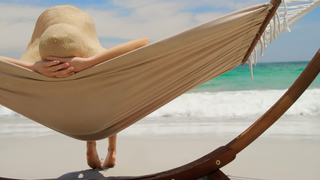 vista trasera de una mujer caucásica relajándose en una hamaca en la playa 4k