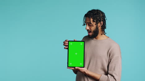 hombre con una tableta de pantalla verde, mostrando emoción positiva, fondo del estudio