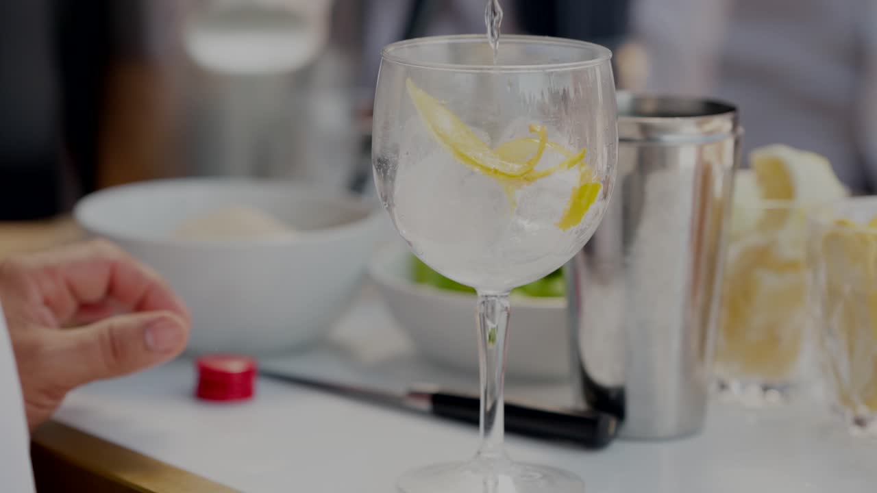 hand holding a glass filled with ice cubes and lemon slices, preparing a cocktail at a gathering.