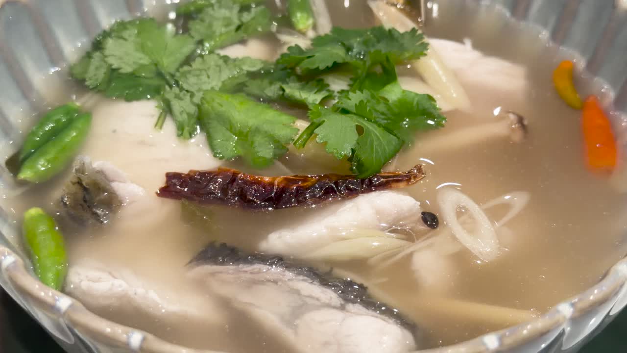 Sea bass tom yum soup with fresh herbs, chili, and clear broth under bright lighting