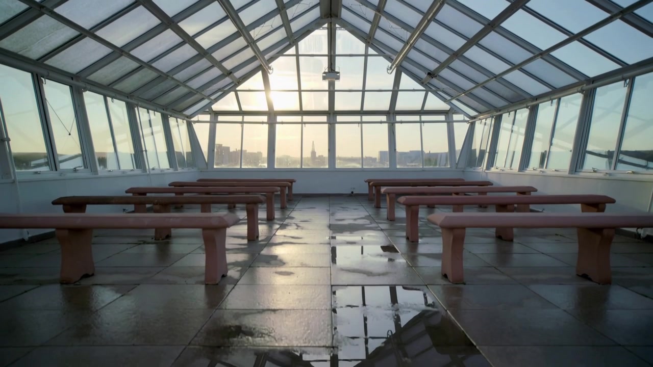 Moving camera revealing glass roof room on rooftop, highlighting wooden benches, puddle reflections