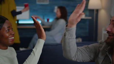 Gemischtrassige-Freunde-Sitzen-Spät-Abends-Im-Wohnzimmer-Auf-Dem-Sofa-Und-Geben-High-Five