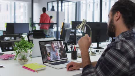 Mixed-race-businessman-sitting-at-desk-using-laptop-having-video-call-with-male-colleague