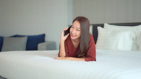 a young woman lying prone on a hotel suite bed talks on her cellphone