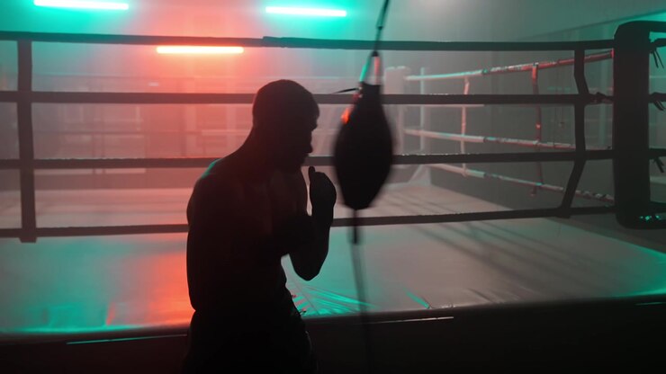 Silueta de boxeador entrenando con saco de velocidad en un gimnasio de boxeo oscuro.