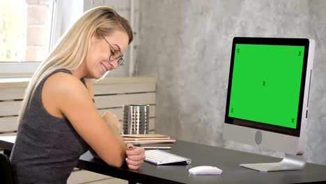 Young woman smiling to camera sitting on her working place. Green Screen Mock-up Display