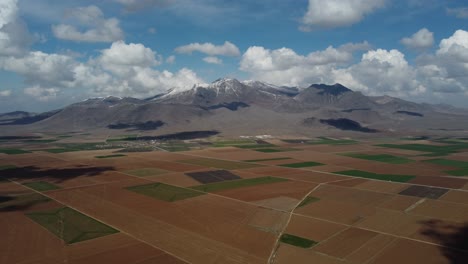 Drone-View-Over-Farmland-Against-Snowy-Mountain