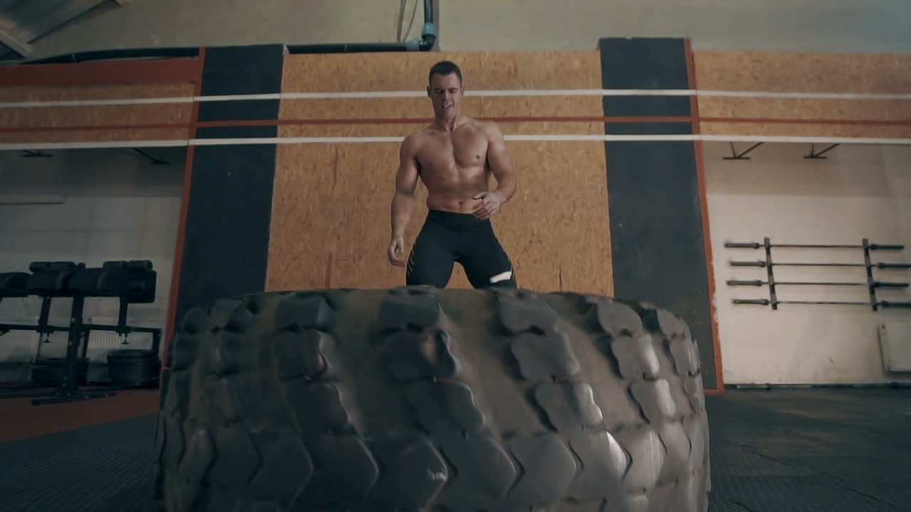 Man Performing Tire Flip Exercise in a Gym