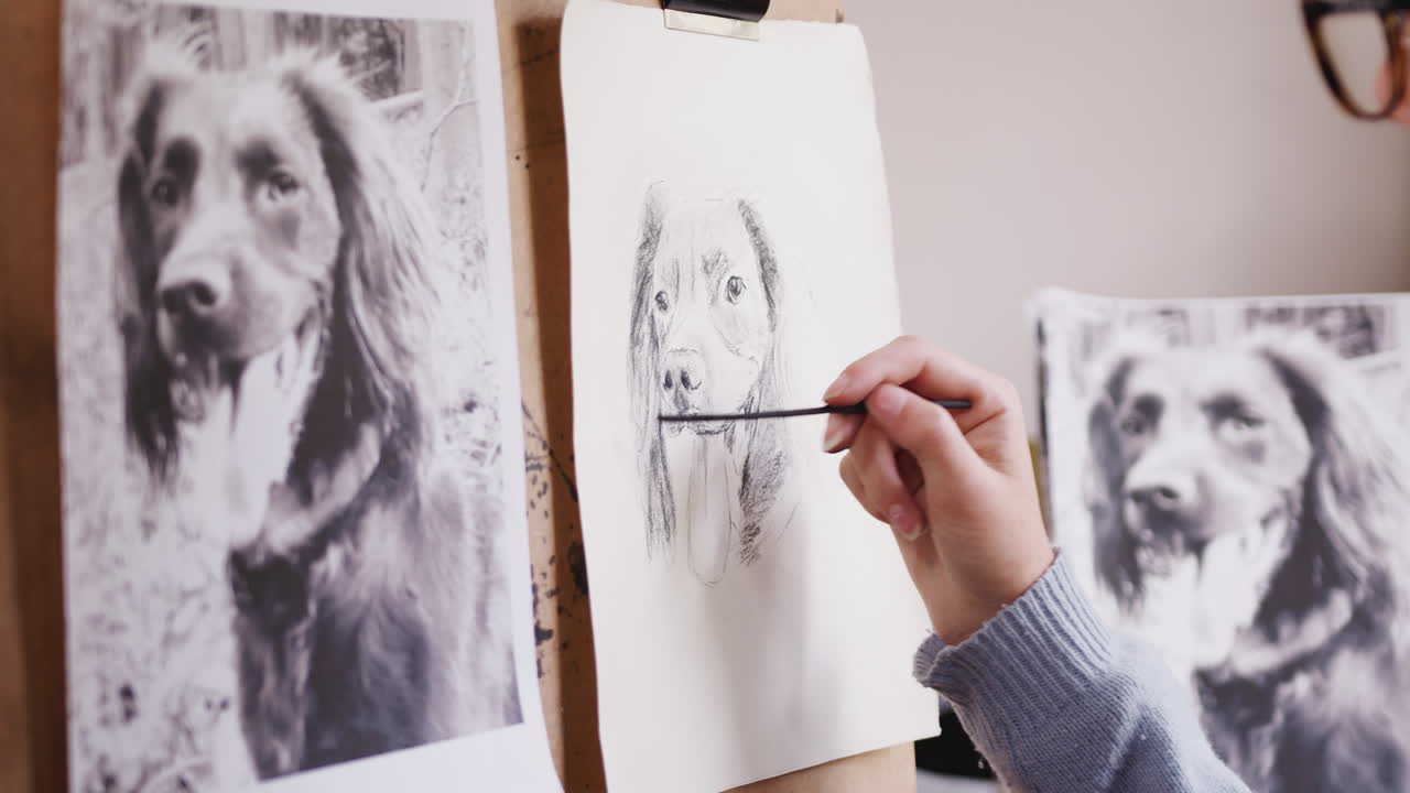 Close Up Of Artist Sitting At Easel Drawing Picture Of Dog In Charcoal From Photograph