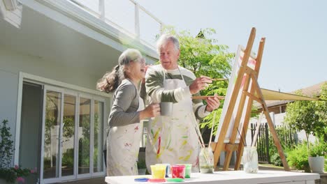 Happy-diverse-senior-couple-painting-in-garden-on-sunny-day