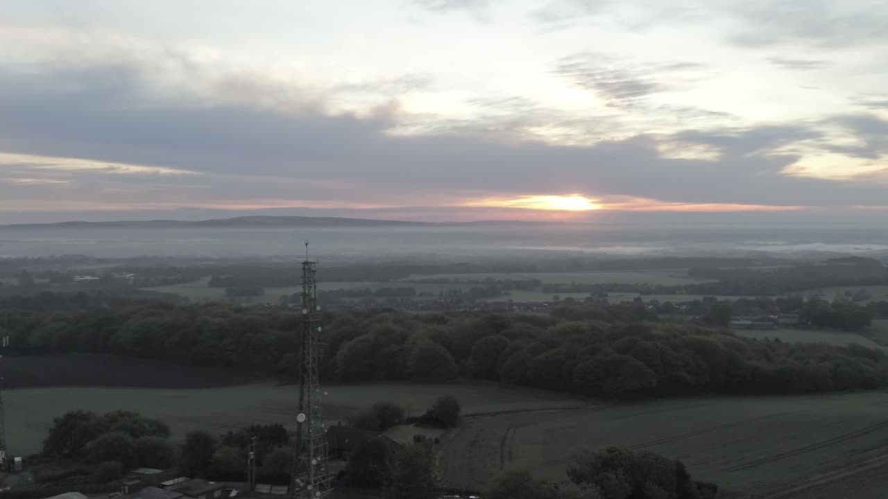 Drone aerial view above British rural farm countryside broadcast signal towers at sunrise slow rising shot