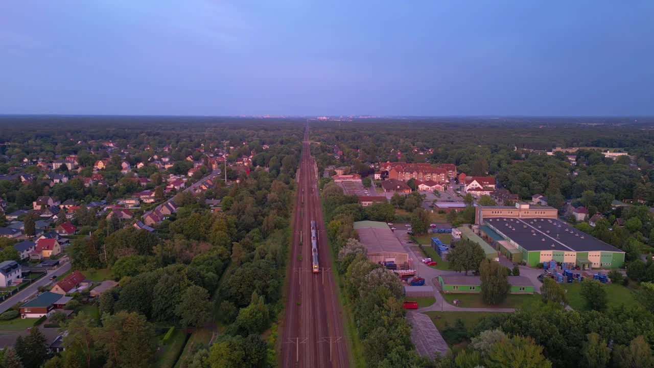 저녁에 작은 마을과 숲을 가로질러 철도로 이동하는 여객 열차.