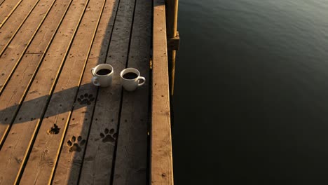 serene morning moments by the water: two coffee cups rest on a wooden dock, highlighting tranquility and connection with nature