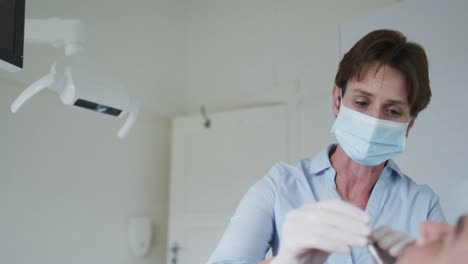 Enfermera-Dental-Caucásica-Con-Mascarilla-Examinando-Los-Dientes-De-Un-Paciente-Masculino-En-Una-Clínica-Dental-Moderna