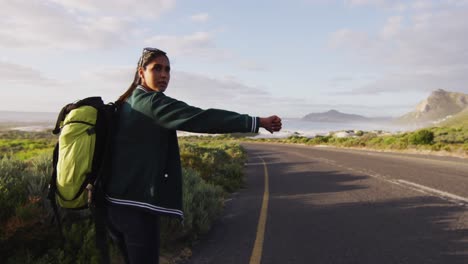 Mujer-Afroamericana-Con-Mochila-Tratando-De-Enganchar-Un-Ascensor-Mientras-Está-De-Pie-En-La-Carretera