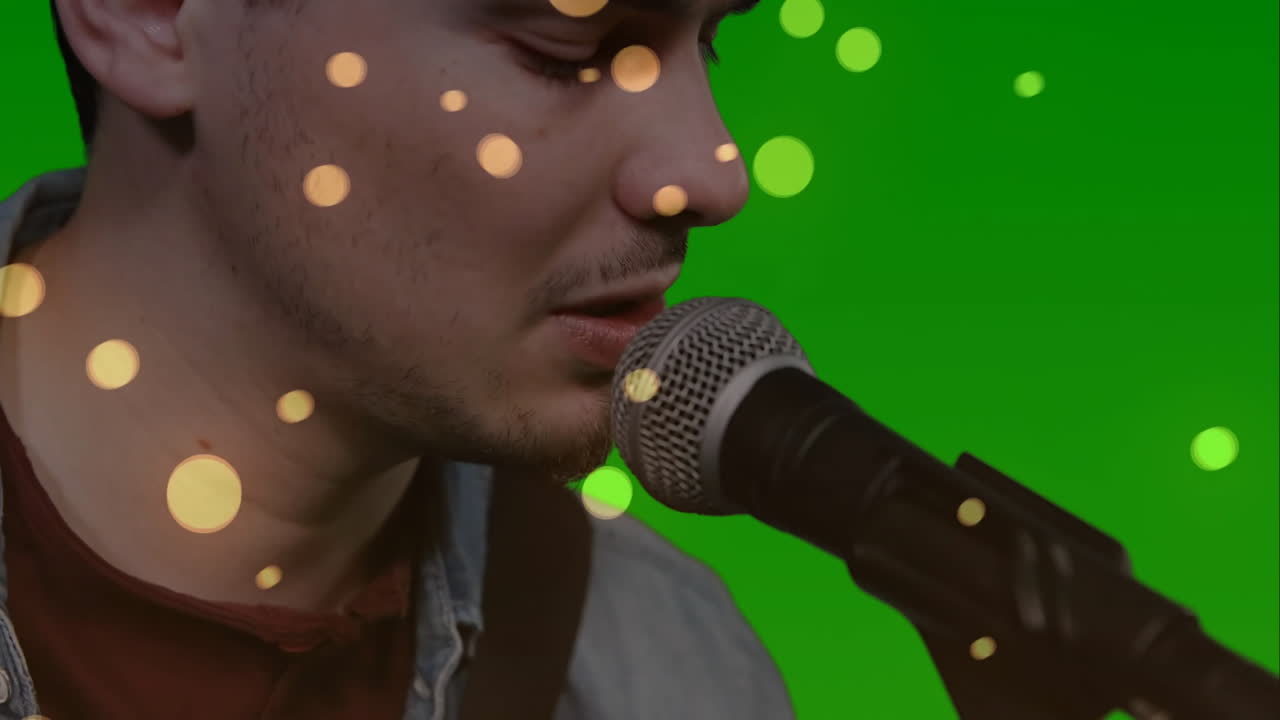 Male singer performing music in studio, showing animated bokeh light overlays on green screen