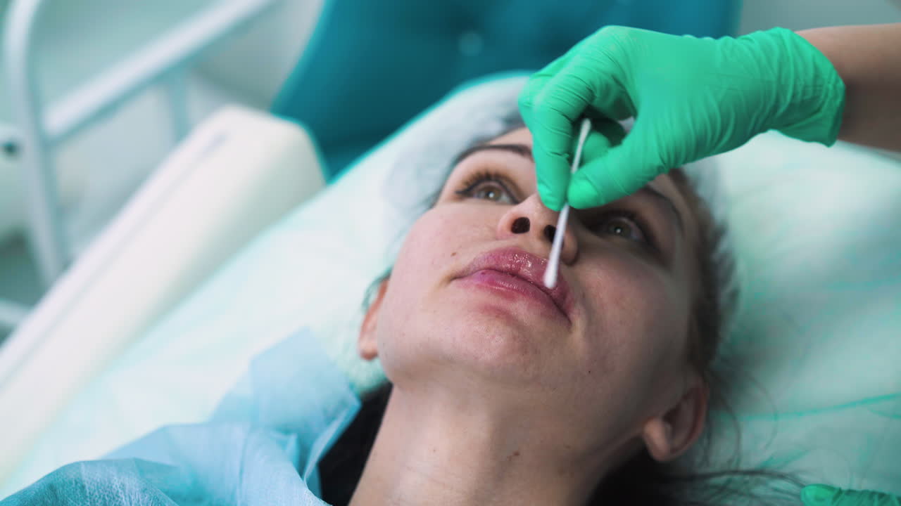la esteticista cubre los labios de la mujer con loción después del aumento
