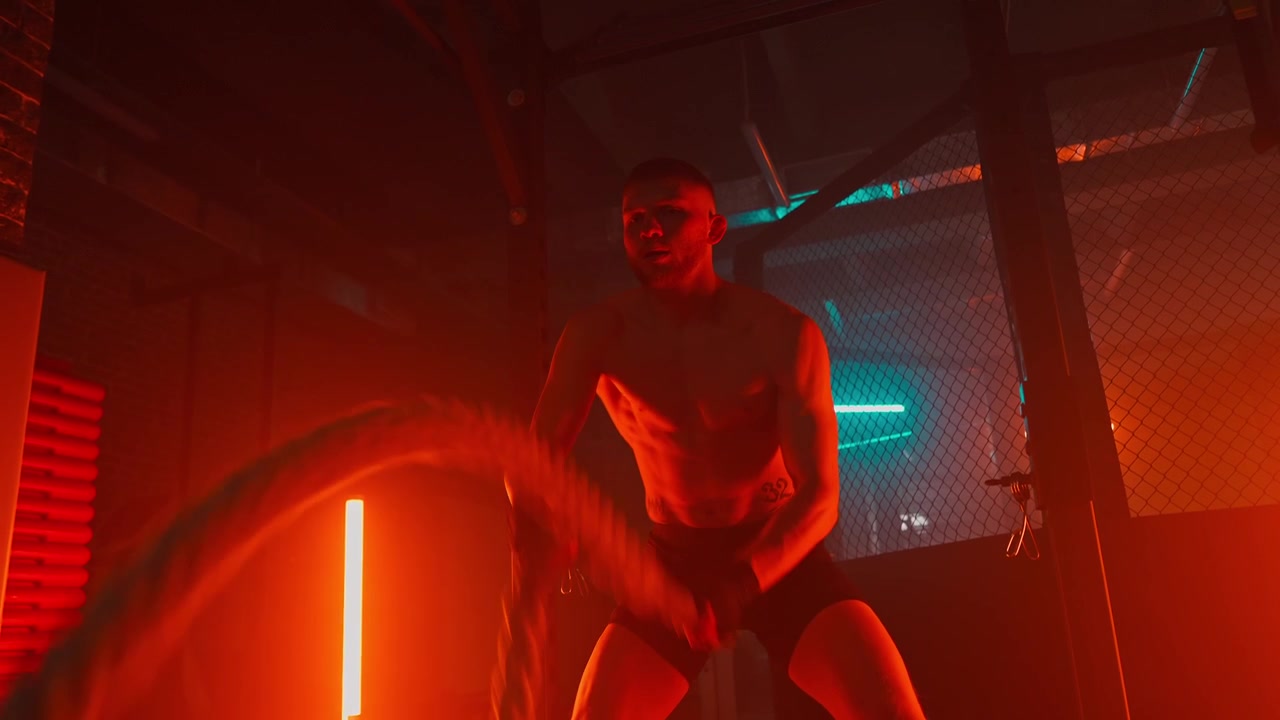 Muskulös man tränar med battle ropes i ett neonbelyst gym