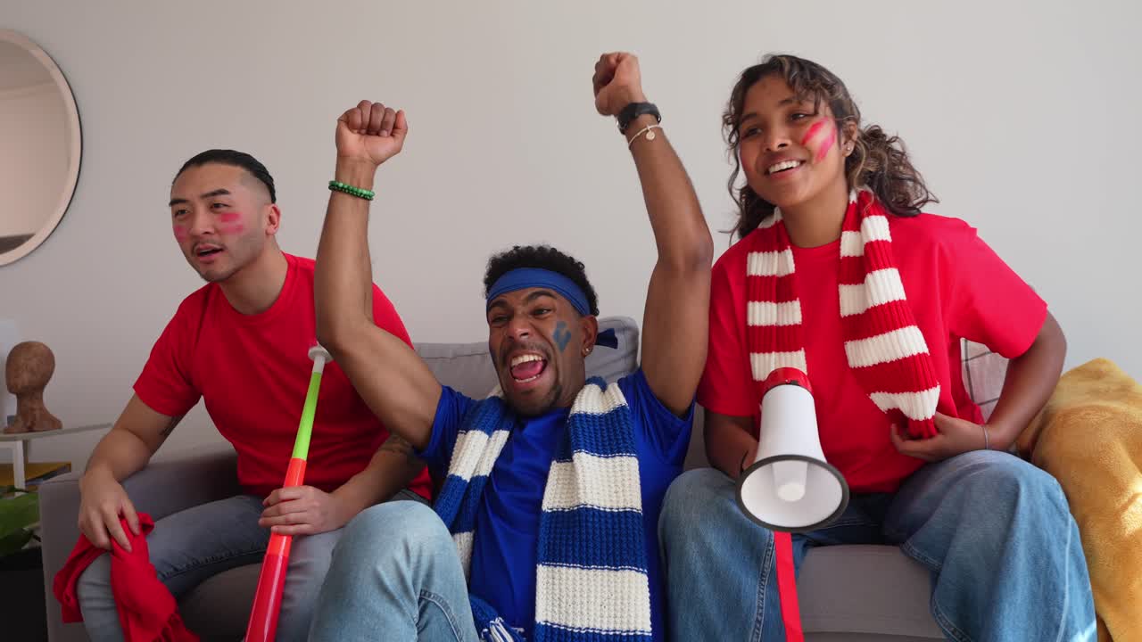 Amigos emocionados viendo un partido de fútbol y animando en casa.