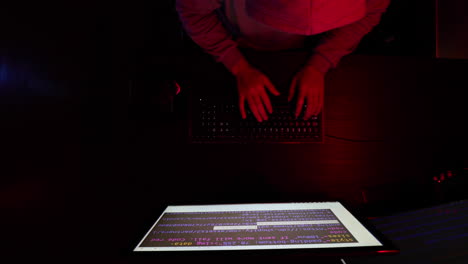 hacker with a hooded sweathshirt and glasses sits down and reads intently to quickly hack a computer by changing the code