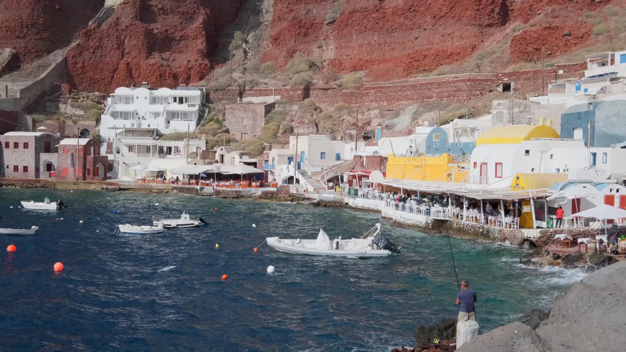 un hombre pescando frente a un pequeño pueblo de cala en santorini