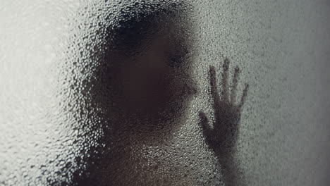 a female silhouette behind the frosted window touches the glass slowly