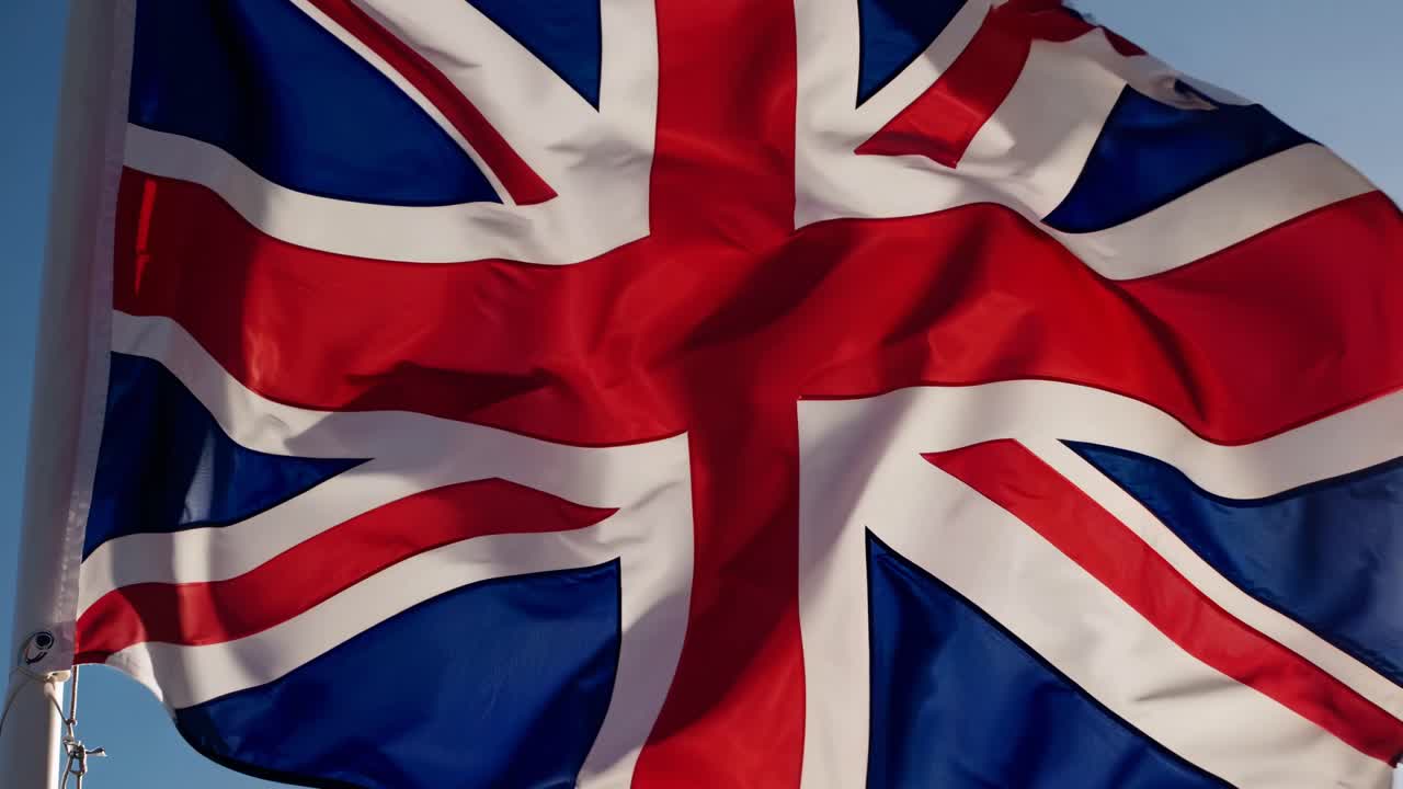A dynamic low-angle video shot of the UK flag waving against a clear blue sky, capturing movement