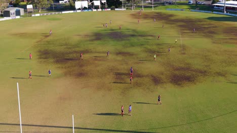 drone footage captures an australian rules football game on a sunny day, highlighting player movements and field dynamics