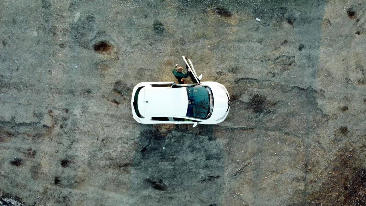 남자가 흰색 전기 자동차에서 내리고 하향식 보기를 걸어갑니다.