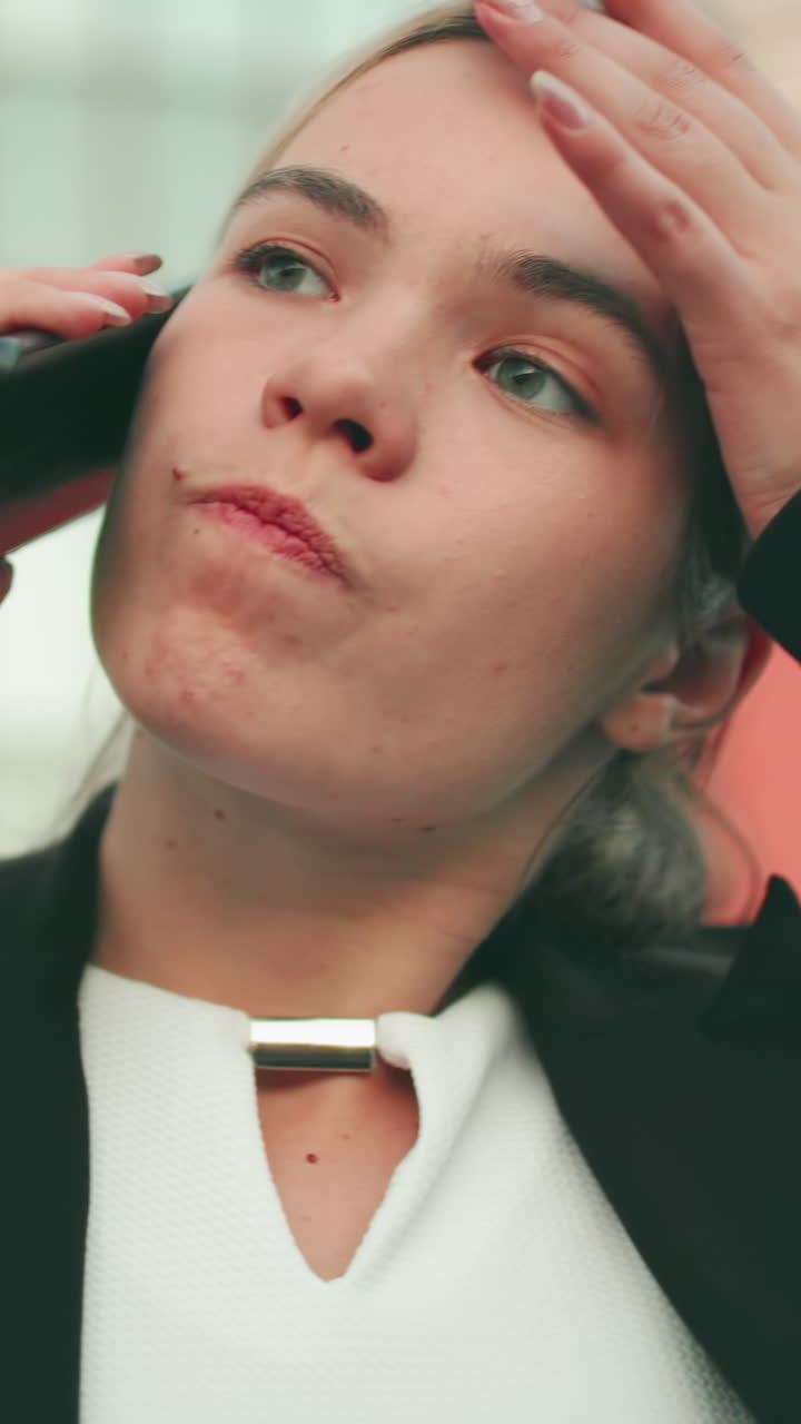 Furious woman in professional outfit stands with arms crossed while on phone call, looking visibly tired and upset in modern urban setting with people blur in distant background