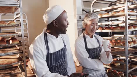 happy diverse bakers working in bakery kitchen, using smartphone in slow motion