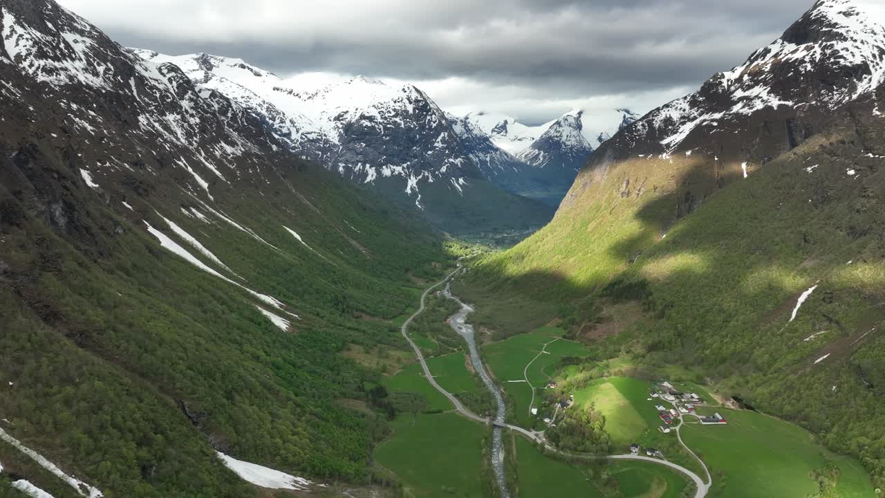 valle de hjelledalen con strynevegen que conduce a la montaña strynefjell - vista aérea de primavera con montañas cubiertas de nieve y manchas de sol en las laderas verdes
