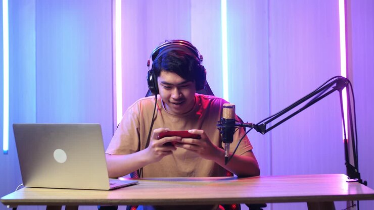 Uomo asiatico eccitato che gioca a un videogioco con il telefono cellulare durante una diretta streaming.