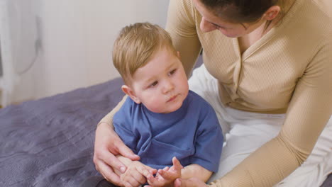 Happy-Young-Woman-Clapping-Hands-And-Playing-With-Her-Baby-Boy-While-Sitting-On-The-Bed-At-Home