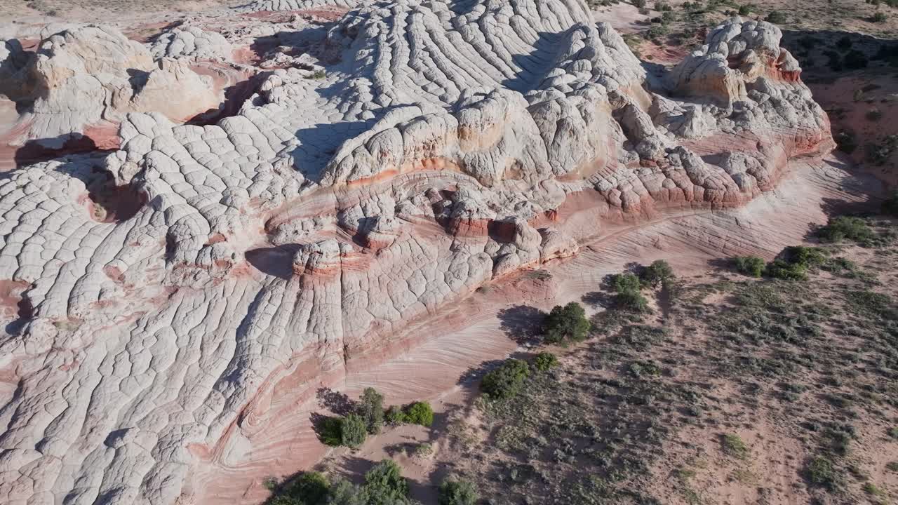 A drone flying backwards and panning up to reveal the unique sandstone features of White Pocket Arizona surrounded by the sandy desert of the Vermillion Cliffs at midday