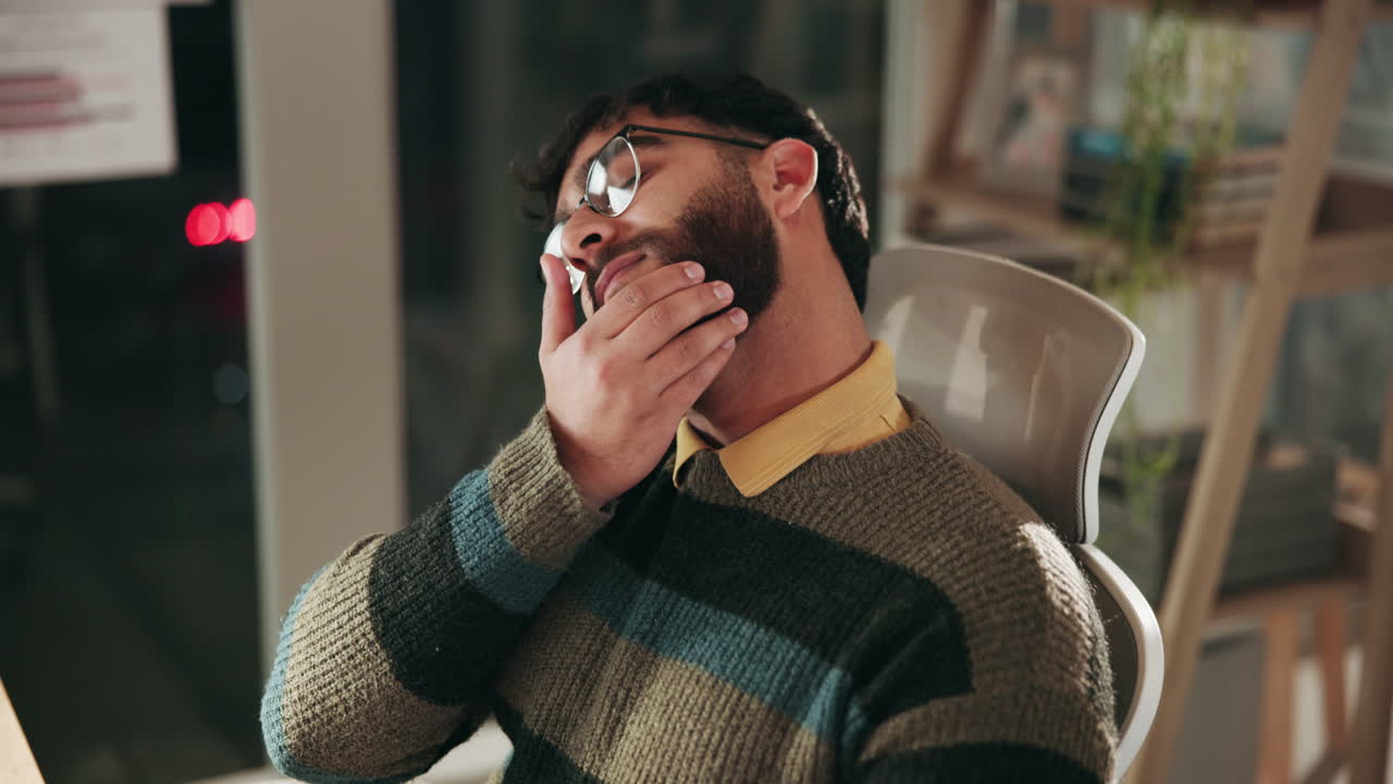 hombre sentado en un escritorio en una oficina, estirando el cuello y mirando cansado