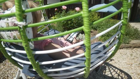 woman reads ebook novel relaxing in comfortable garden hammock on hot sunny day