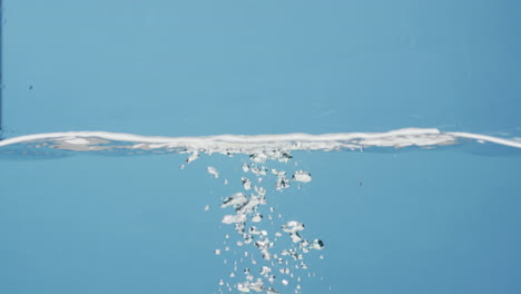 video of beauty product bottle walling into water with copy space on blue background