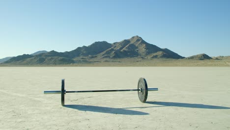 slow motion barbell with weights sitting in empty dry lake bed