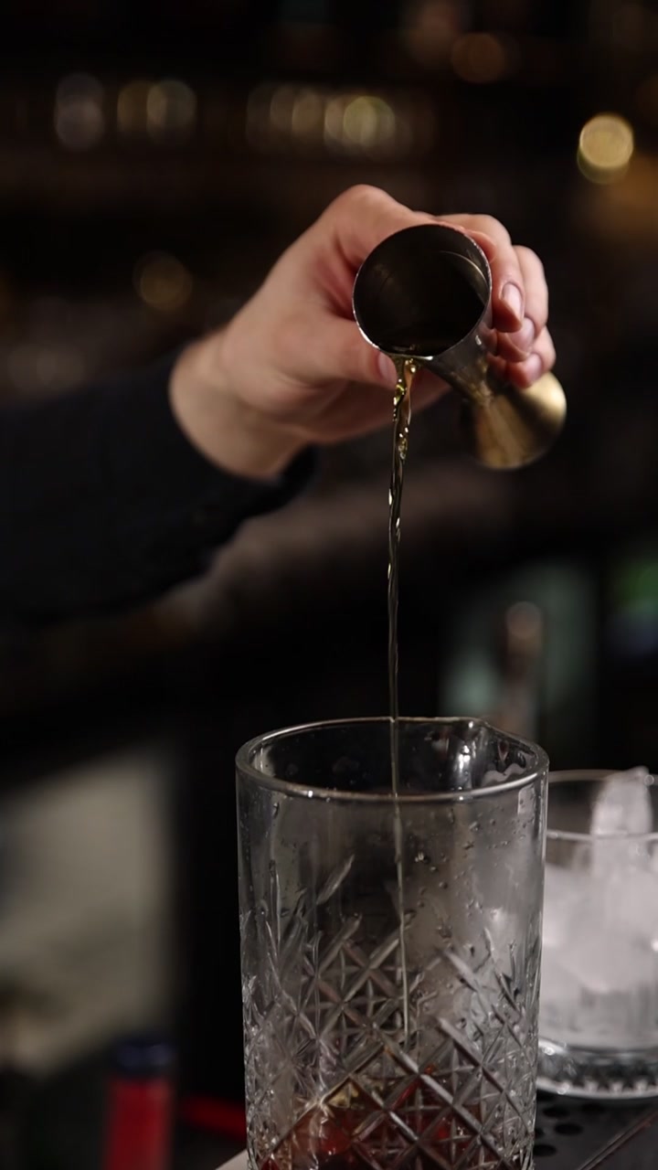 Barman che versa alcol dosato da un misurino in un bicchiere da cocktail