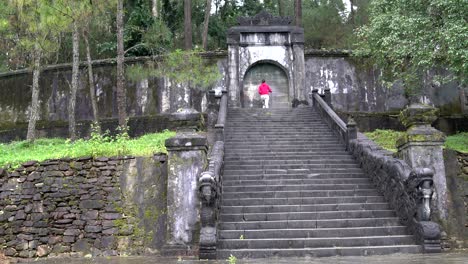 a woman climbs the stone stairs to the gate and knocks at them