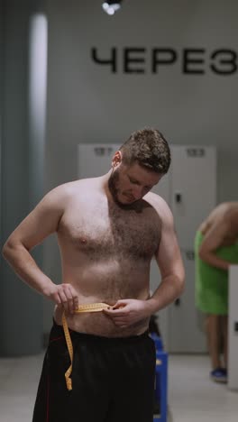 man measuring waist in a gym locker room