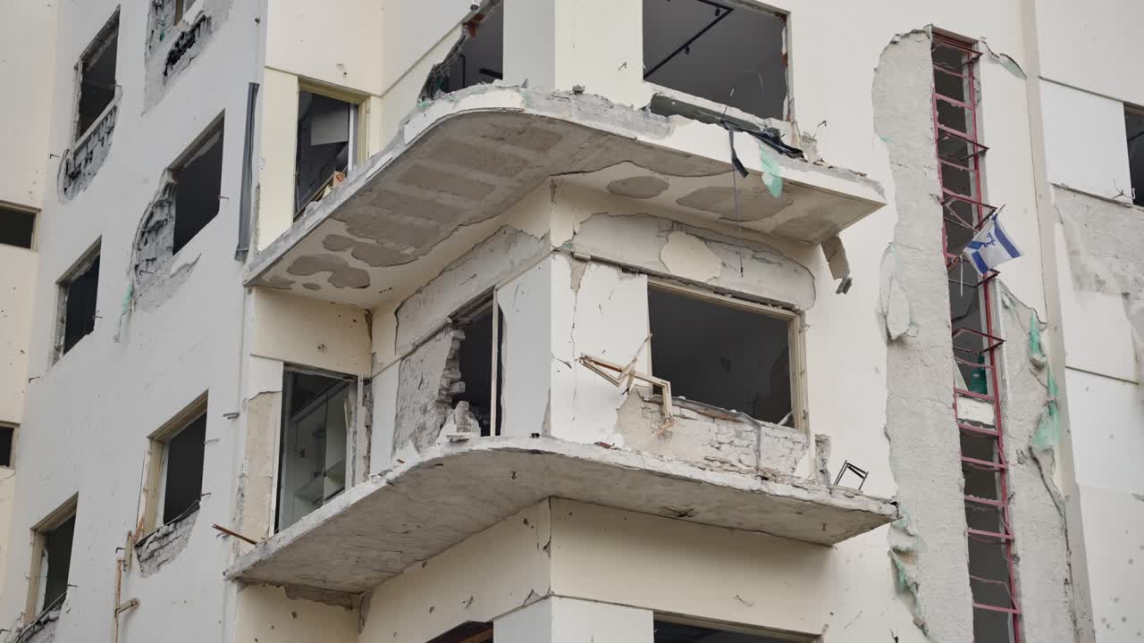 Heavy blast damage residential building. broken windows, cracked walls, exposed rebar and ruined balconies. news reports, conflict aftermath, disaster response, reconstruction and humanitarian stories