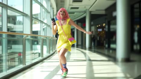 a vibrant performance: a person in a colorful dress and pink hair dancing and enjoying music in a modern shopping mall setting