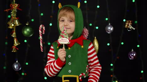 Kid-girl-in-Christmas-elf-Santa-Claus-helper-costume-licking-candy-lollipop-caramel-sweets