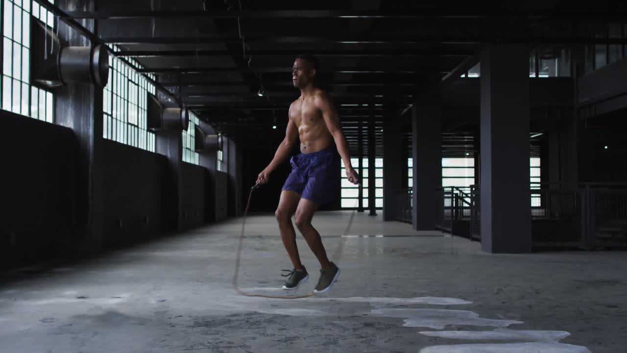 Shirtless african american man skipping the rope in an empty urban building