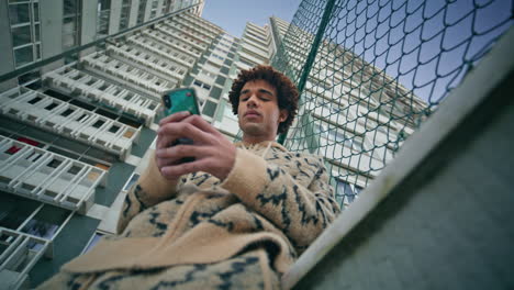 street hipster using smartphone by city fence focused on screen. latin guy
