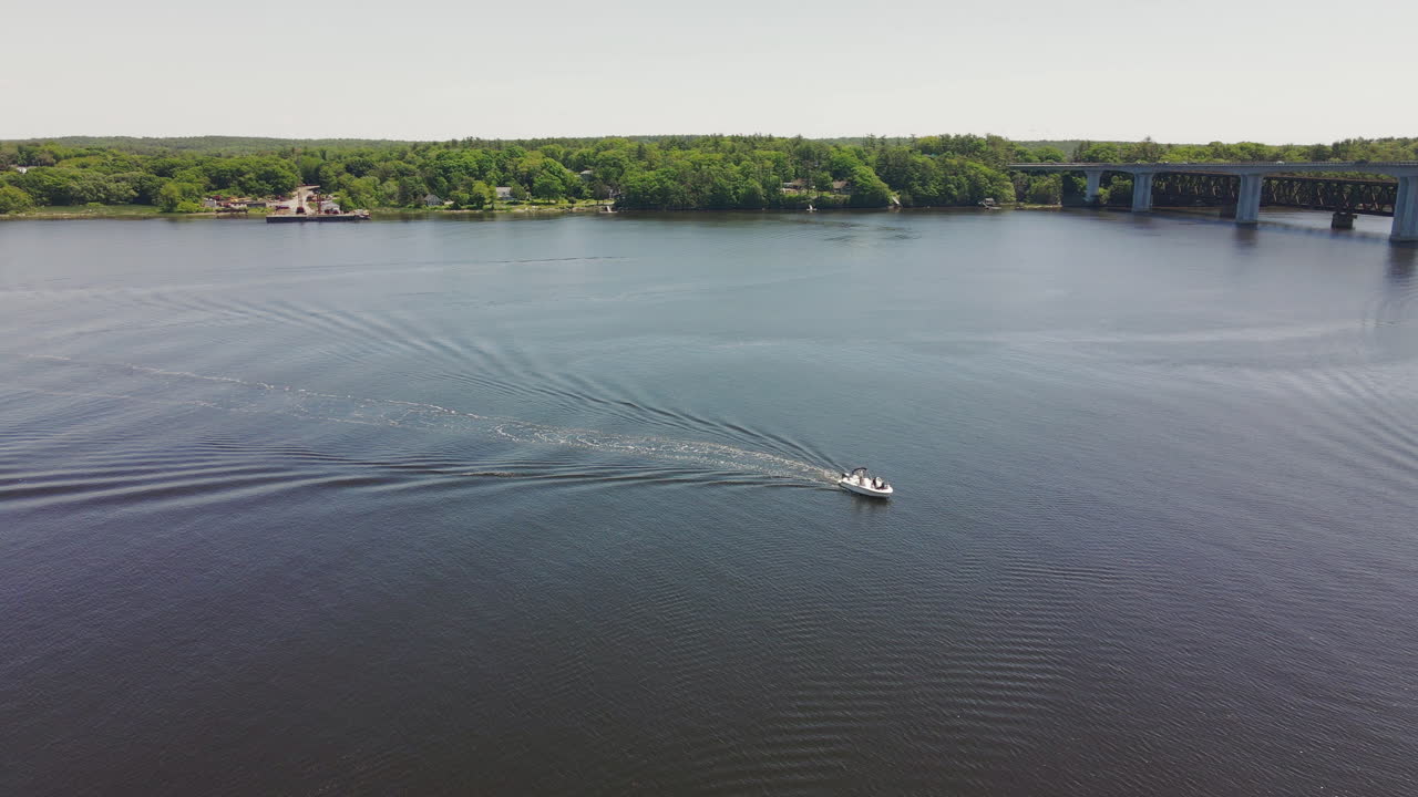 A boat cruising on a river with a bridge and treelined shore in the background