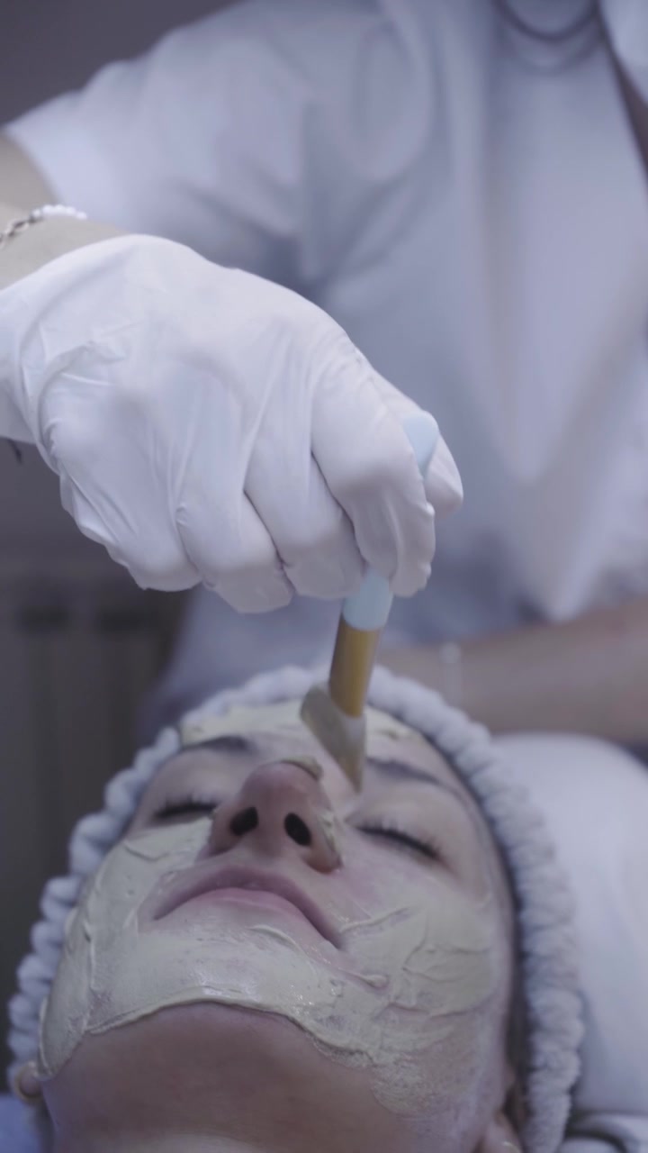 Delicate pennellate applicano una maschera d'argilla lungo la guancia in un rituale viso rilassante