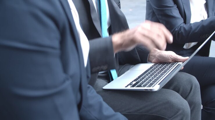 Primo piano di un uomo d'affari irriconoscibile con un laptop, seduto all'aperto vicino a partner o colleghi e che parla